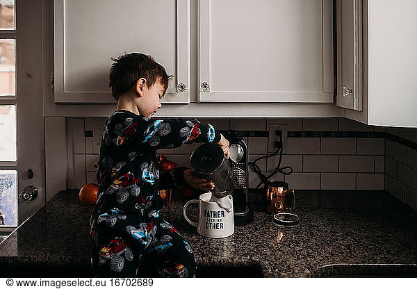 Young boy in kitchen pouring milk into coffee cup for dad