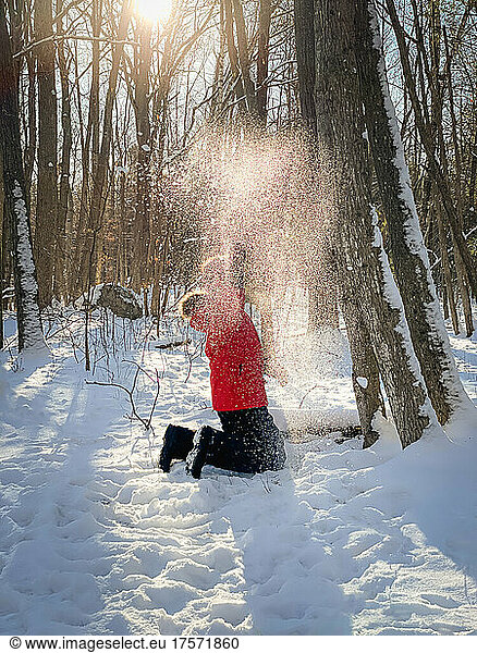 Young boy in red winter coat playing in the snow in the woods.