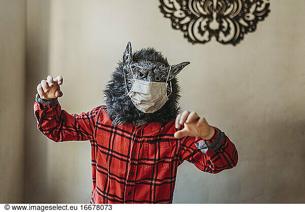 Young boy in wolf mask with face covering over mask standing at home