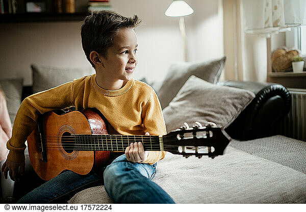Young boy in yellow sweater playing the acoustic guitar at home.