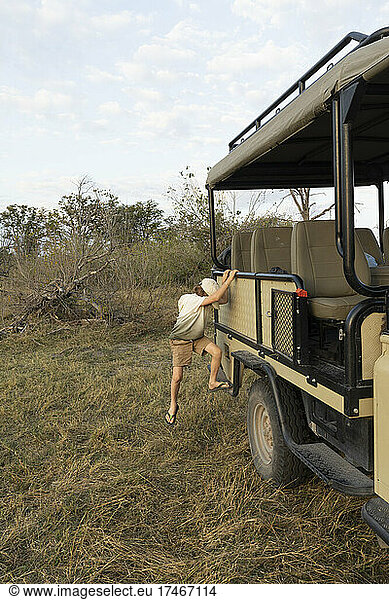 young boy jumping from safari vehicle  Okavango Delta  Botswana