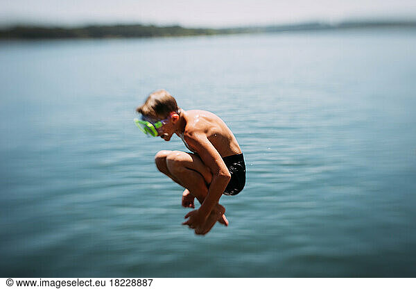 Young boy jumping into lake on summer day