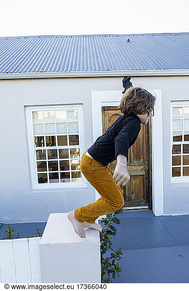 Young boy jumping off a low wall outside a house