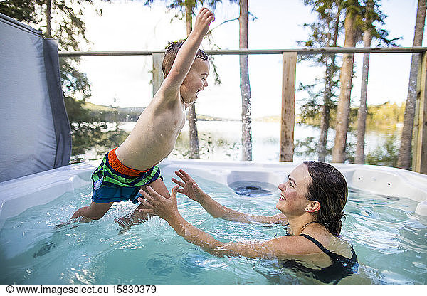 young boy jumping to mother in hot tub during vacation.