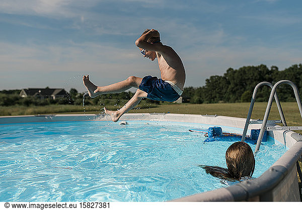 Young boy jumps into pool on a sunny summer day in the backyard