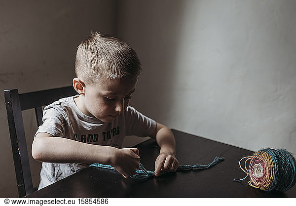Young boy knitting with fingers at home during isolation