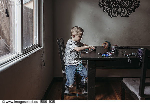 Young boy knitting with fingers at home during isolation