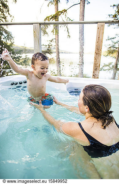 Young boy laughing and smiling with swimming ans splashing in pool.