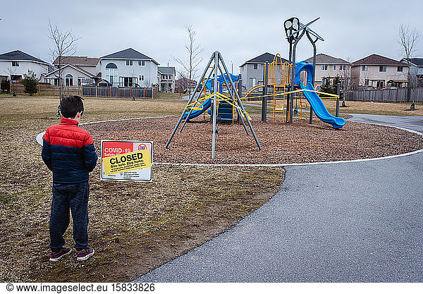 Young boy looking at closed playground during Covid 19 pandemic.