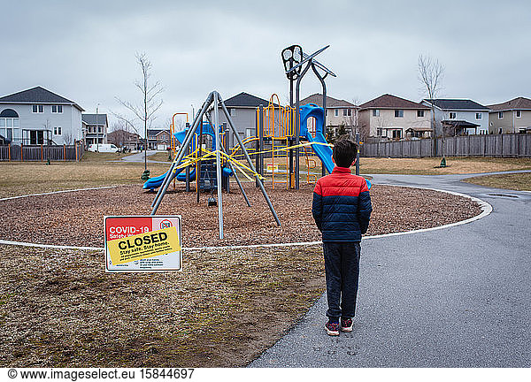 Young boy looking at closed playground during Covid 19 pandemic.