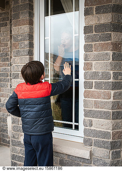 Young boy looking through window at grandma during Covid 19 pandemic.