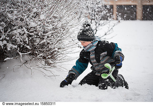 Young boy making snowball with snowball making toy on winter day.