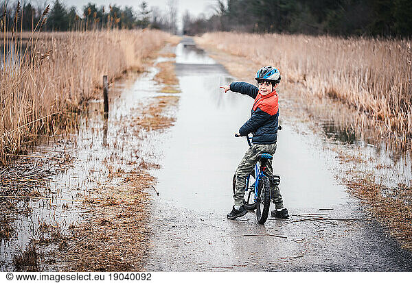Young boy on a bike pointing to a flooded section of biking trail.