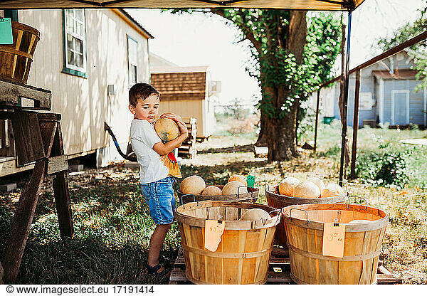 Young boy outside holding fresh cantaloupe at local farmers market