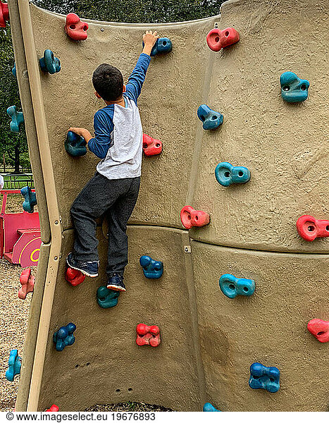 Young boy playing on climbing wall suburban playground.