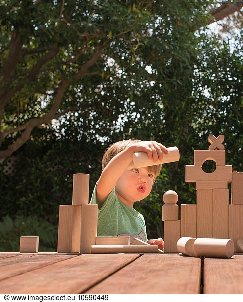 Young boy playing with wooden building blocks in garden