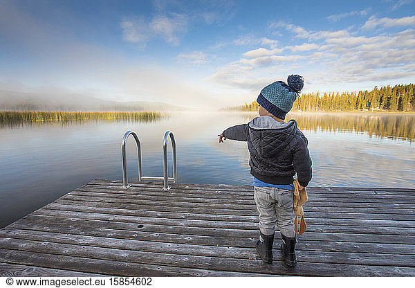 Young boy pointing at water from wooden dock.