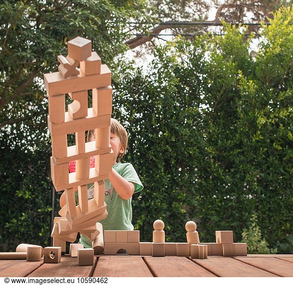 Young boy pushing over wooden structure made from building blocks  outdoors