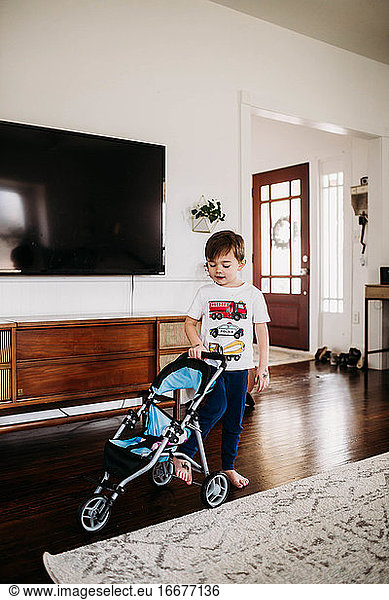 Young boy pushing stroller with stuffed animal in livingroom