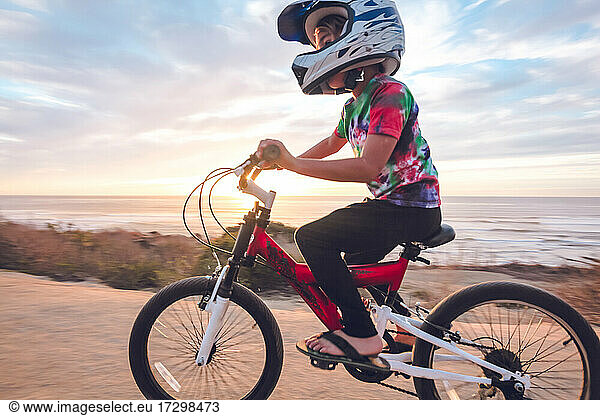 Young boy riding his bike on a coastal trail at sunset.