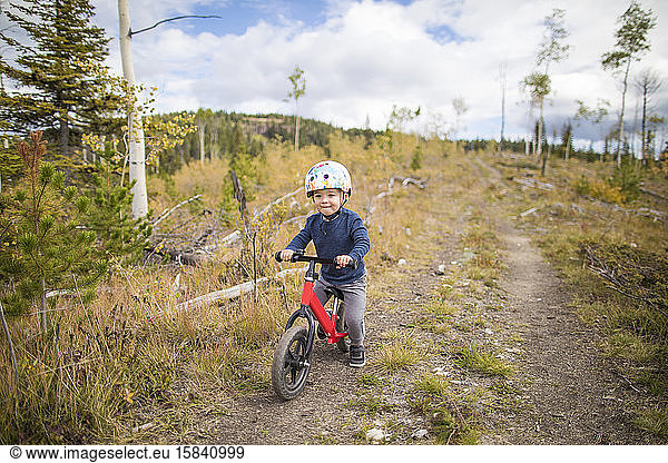 Young boy riding red bike on dirt pathway through forest.