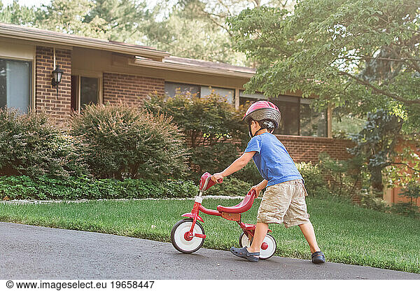 Young boy riding tricycle on suburban driveway.