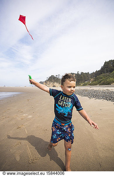 Young boy running kite along the beach with determination.