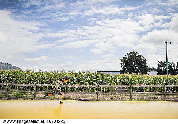Young boy running on large yellow trampoline at rural farm.