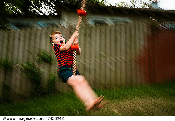 Young boy shouting with joy on rope swing in motion.
