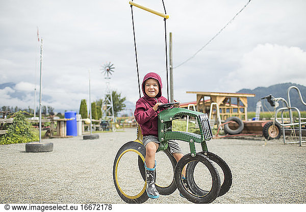 Young boy sits on play ride on tractor at farm.