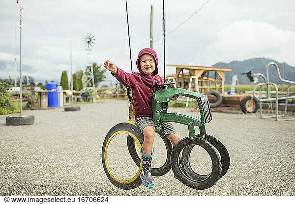 Young boy sits on play ride on tractor at farm made from recycled tire