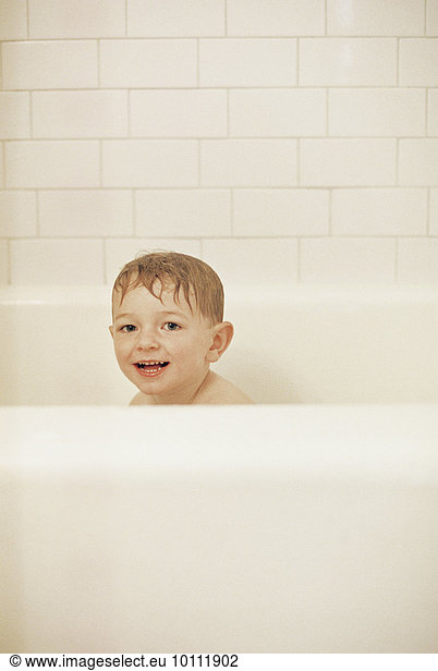 Young boy sitting in a bathtub  having a bath  smiling at camera.