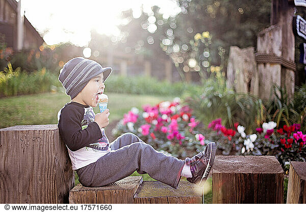 Young boy sitting on a fence and eating ice cream.