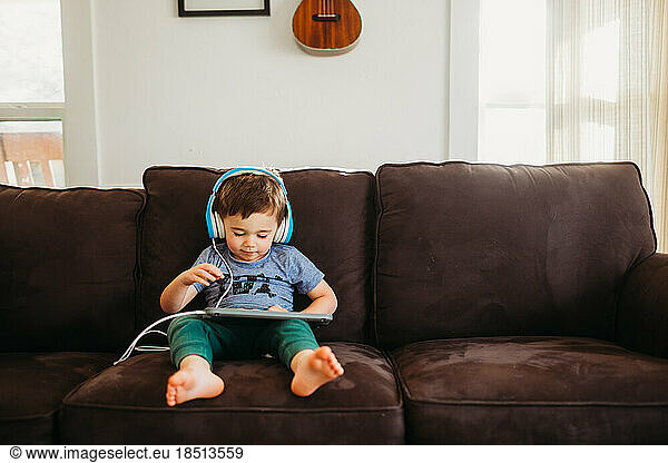 Young boy sitting on couch using tablet and wearing headphones