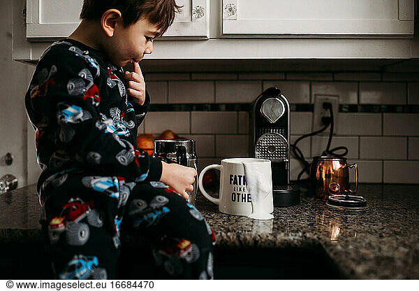 Young boy sitting on counter top with spilled milk on coffee cup