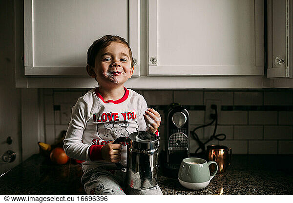 Young boy sitting on kitchen counter with frothed milk on face