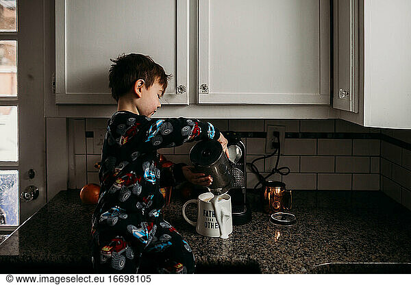 Young boy sitting on kitchen couter spilling milk on coffee mug