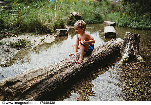 Young boy sitting on log in water in summer looking thoughtful
