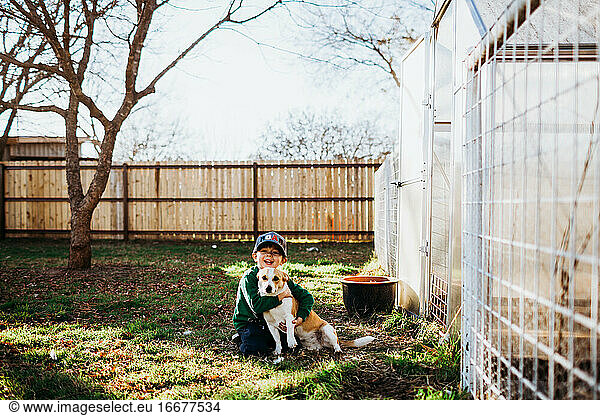 Young boy smiling and hugging dog in backyard during spring