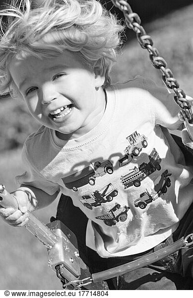 Young Boy Smiling Swinging In A Swing At The Playground.