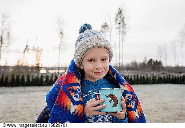 young boy smiling whilst wrapped in a blanket holding a hot chocolate