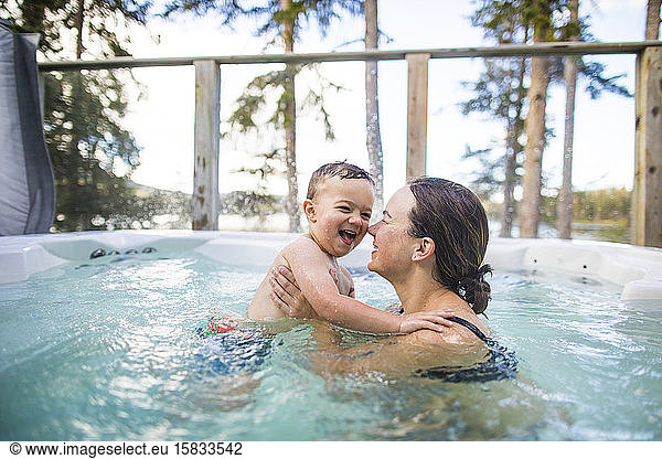 Young boy splashing and playing with mother in swimming pool