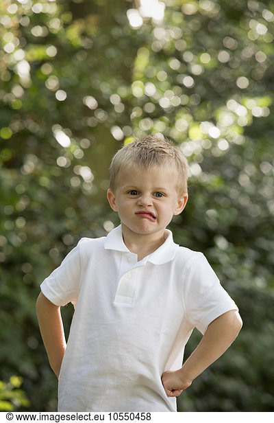 Young boy standing in a forest  looking at the camera  pulling a face.