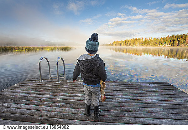 Young boy standing on dock looking out over calm lake