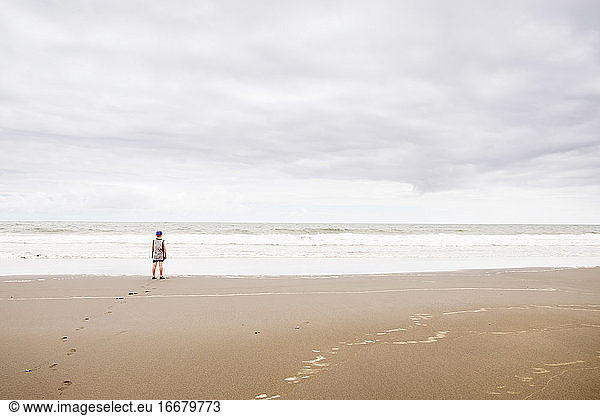 Young boy standing on the beach looking at the water