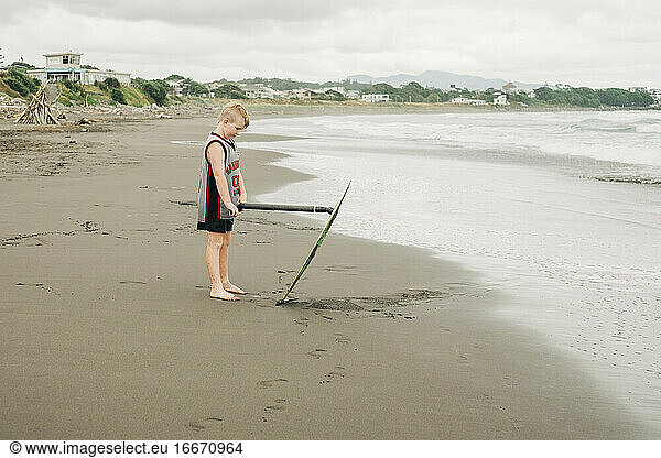Young boy standing on the beach with his skim board