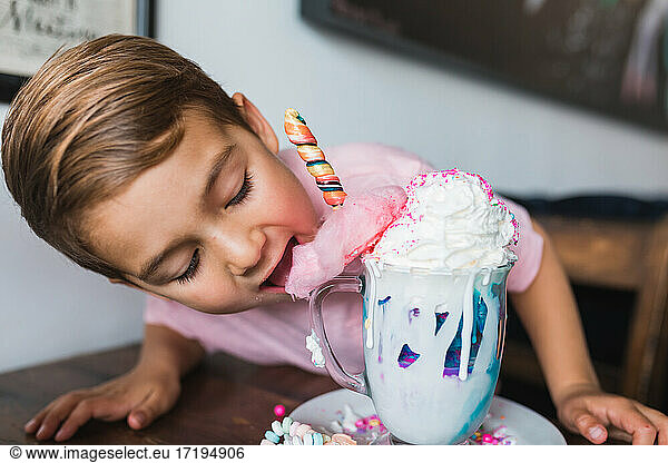 Young boy taking a bite of cotton candy on top of a milk shake.