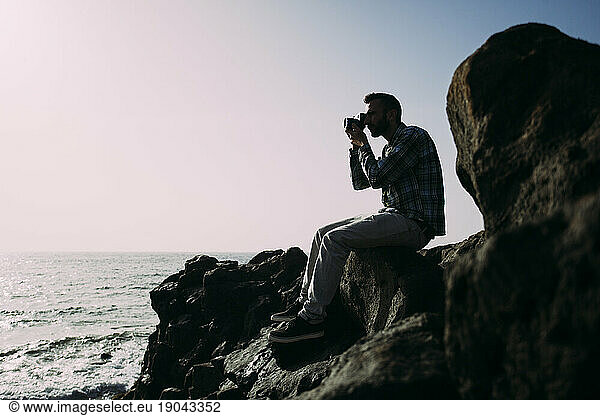 Young boy taking pictures in backlight beside the sea.