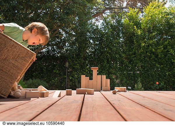 Young boy tipping wooden building blocks out on garden decking
