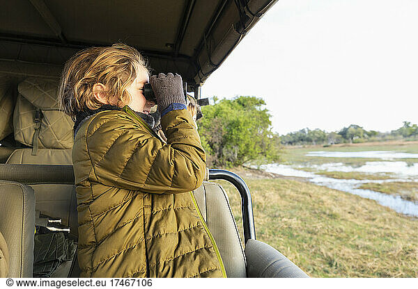 Young boy using binoculars standing in a safari jeep.